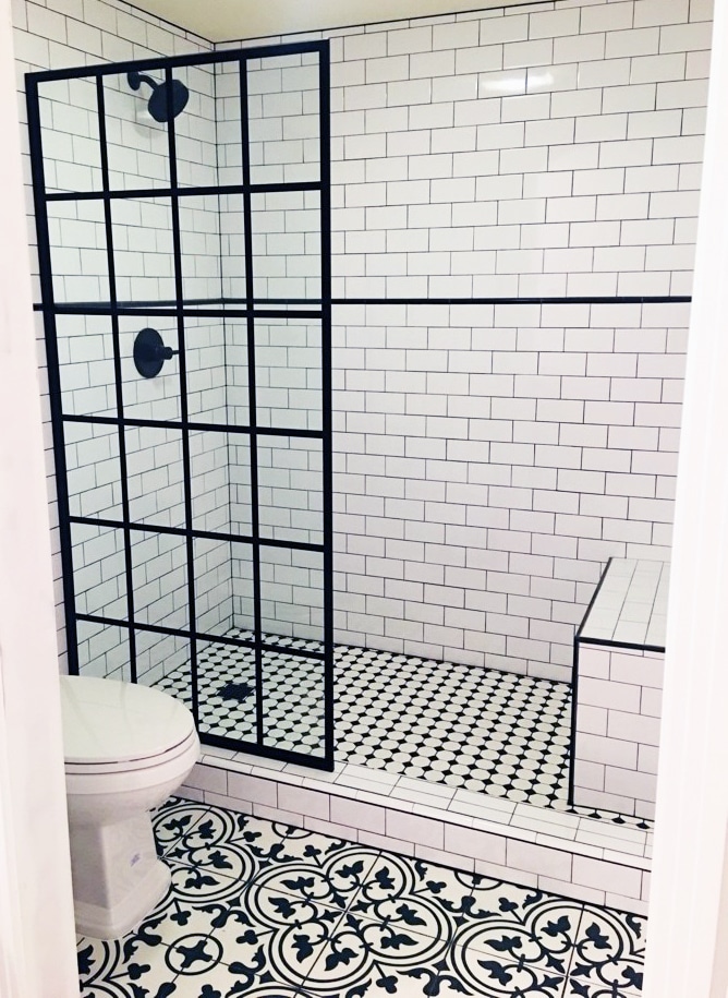 Classic to a Luxurious Aesthetic. Encaustic style black and white tile flooring and white subway tile with black grout work. The shower features black trim details and accessories.