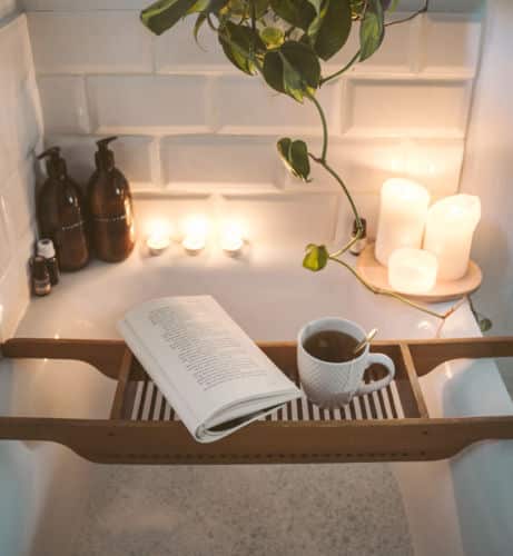 A bathroom transformed into an at-home spa with a tub tray, candles, and plants.