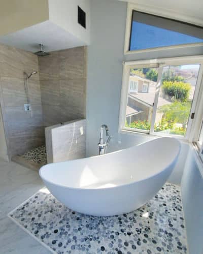 Stand alone slipper bathtub set above blue penny tiled flooring, to section it off. 