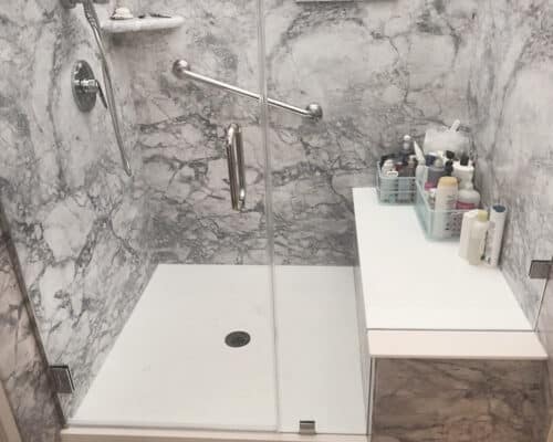 A built in shower bench  / seat in a newly renovated marble patterned shower. There are soap and shampoo bottles placed on the bench. 