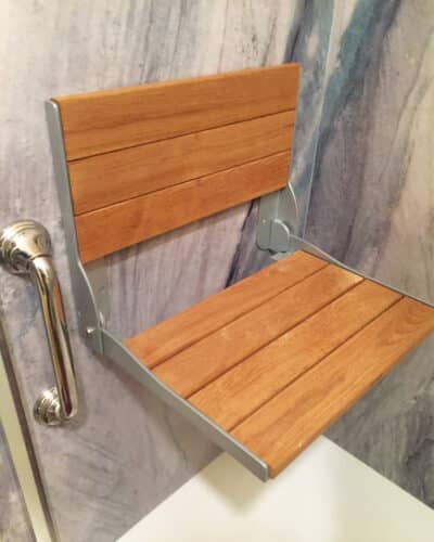 A teak wood folding shower seat installed on a shower wall.