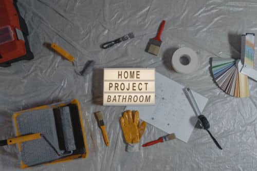 5 Helpful Bathroom Remodeling Tips - Remodeling tools like paintbrushes, paint samples and gloves are set next to a small marquee sign that reads: " Home Project, Bathroom"