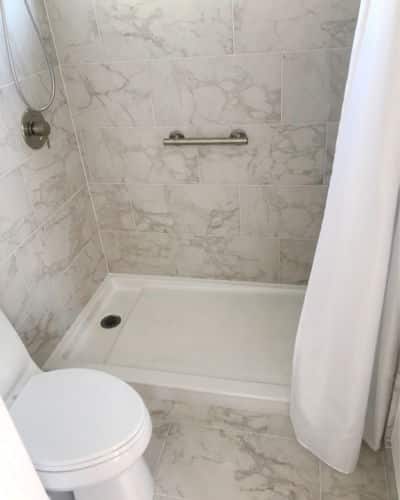 low and no threshold. Shower. A Low threshold shower pan. Shower walls and bathroom floor are covered with marble tile. 