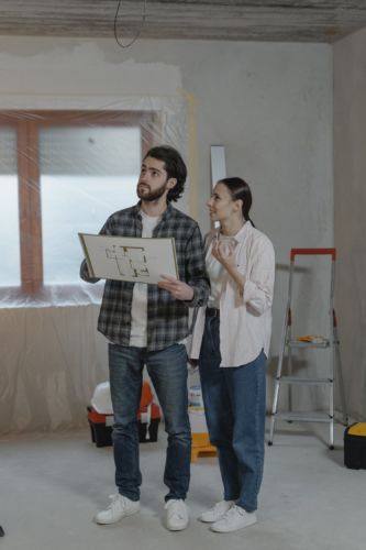 5 Helpful Bathroom Remodeling Tips- Picture is a man and woman, holding a blueprint design as they look up towards the ceiling.
