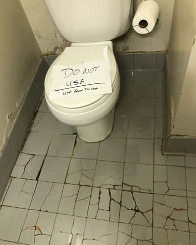 Scary Bathroom - a toilet surrounded by damaged, broken tile flooring. There's a sign on the toile tthat reads "do not use. use other bathroom."