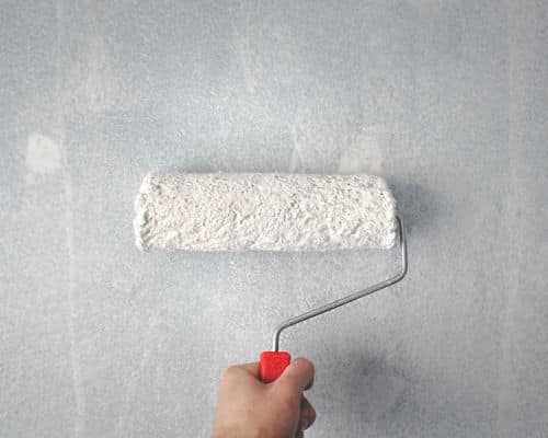 Best Bathroom Paint - A paint roller is being held against a wall. The roller is covered in white paint and the wall is lightly coated. 