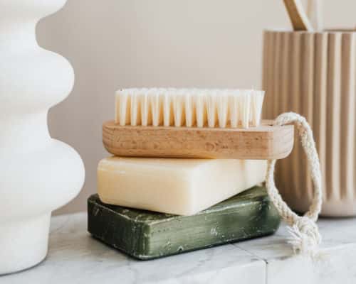 Items Your Shouldn't Store in Your Bathroom: A bar of soap is set atop a green soap holder. On top of the soap is a scrub brush. 