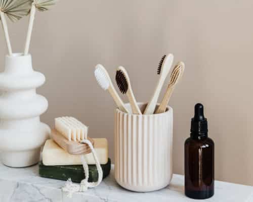 Items Your Shouldn't Store in Your Bathroom: A containing 4 wooden toothbrushes, sets on a marble ledge, next to a glass serum bottle and a bar of soap.