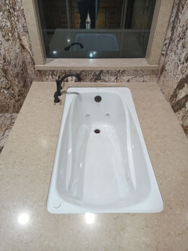 TYPES OF BATHTUBS: a white undermount tub is placed beneath a beige surround frame.