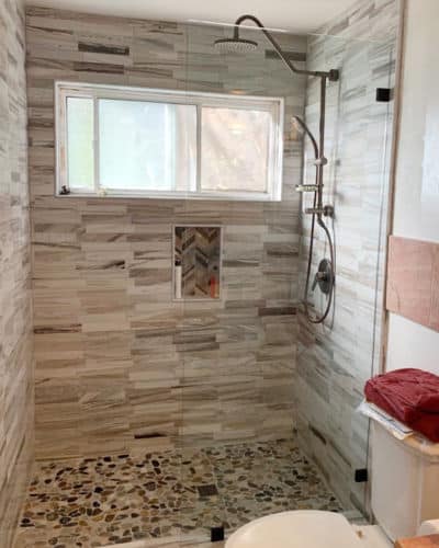 8 Before and After Bathroom Remodel Photos : A remodeled walk-in shower with brown pebbled tile base and a variation of brown tiles on the walls.